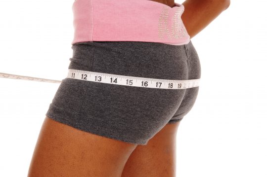 A young african american woman in a closeup image of her bottom, measuring her bum, isolated for white background.